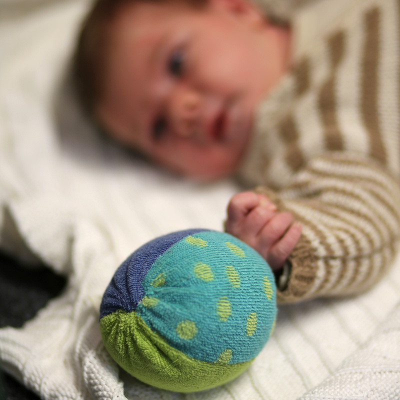 Baby greift nach einem bunten Stoffball auf einer weißen Decke